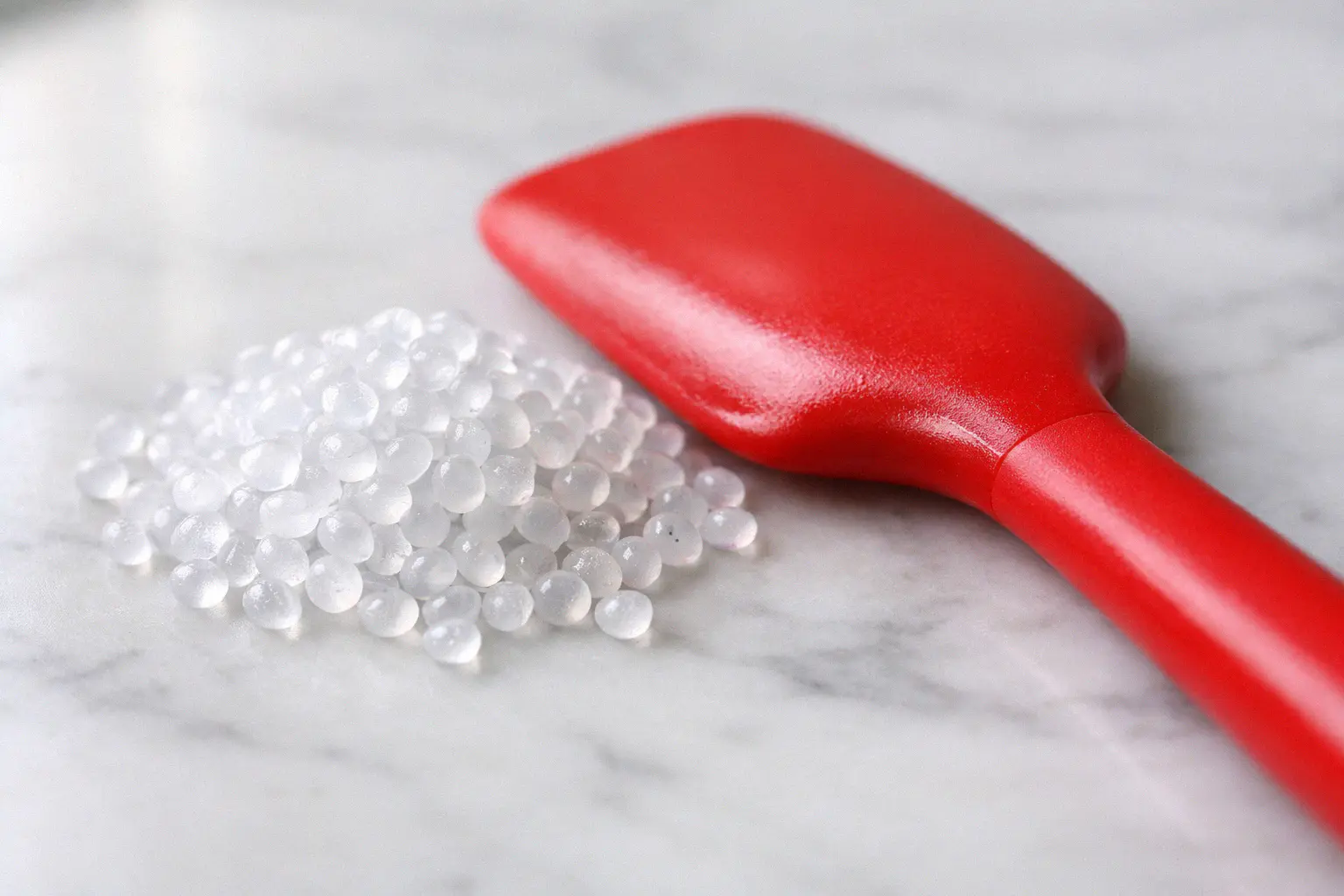 Food grade silicone pellets next to a finished silicone kitchen spatula showing material purity
