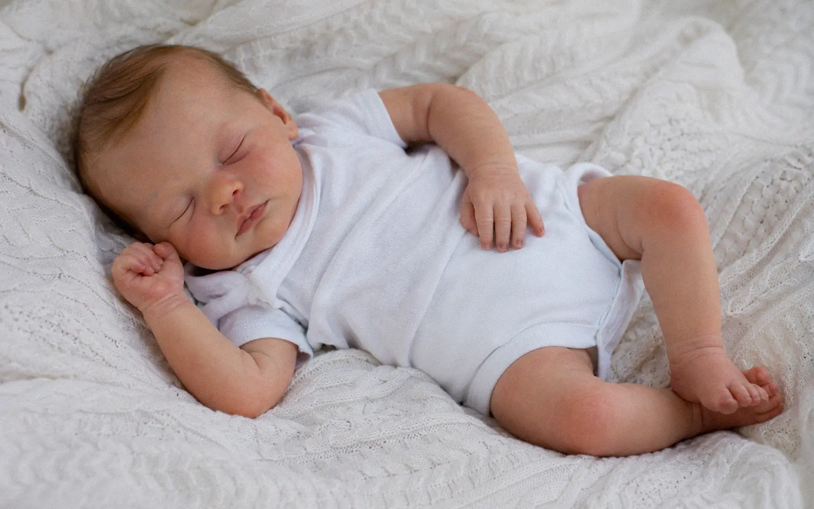Completed handmade silicone baby doll with realistic skin tones, rooted hair, and glass eyes lying on a white blanket