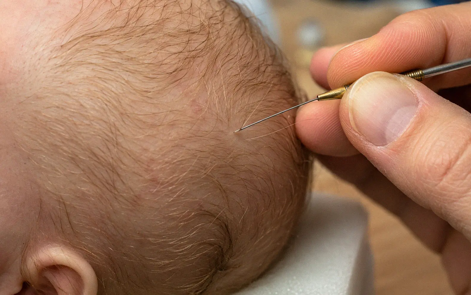 Close-up of a rooting needle inserting individual mohair strands into a silicone baby doll scalp