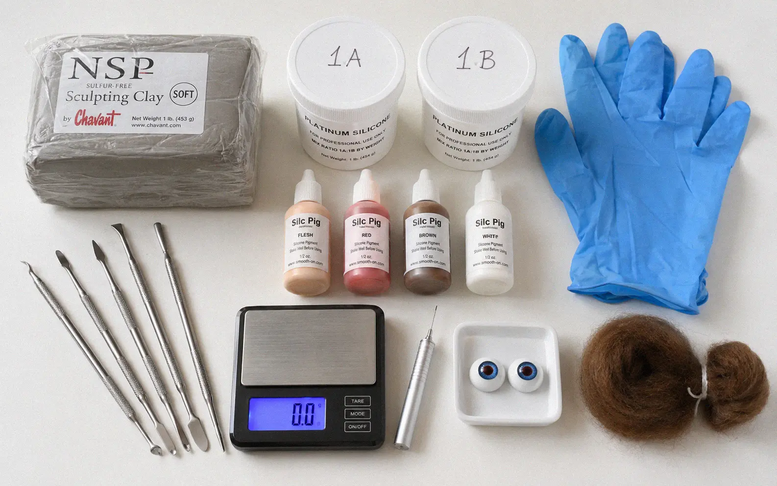 Silicone baby making supplies laid out on a workbench including clay, pigment bottles, mixing cups, and tools